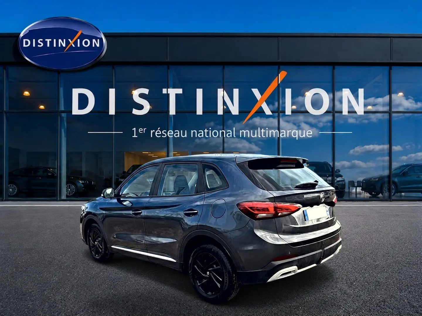 Vue 3/4 arrière droite du MG ZS Camden grey 2026 avec feux LED et jantes noires devant un showroom Distinxion.