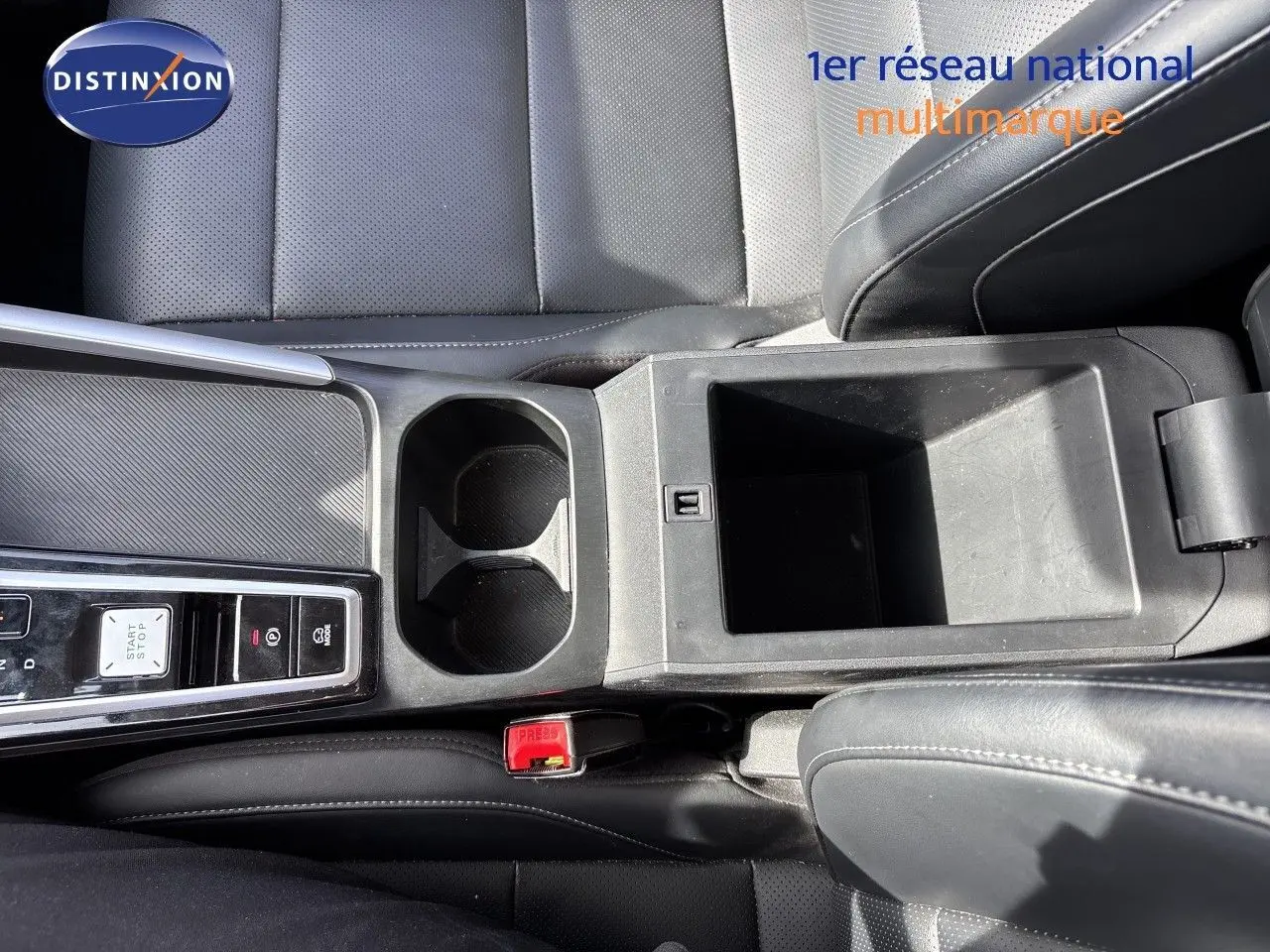 Vue plongeante sur la console centrale noire du MG ZS 1.5L Hybrid+ 2025, avec porte-gobelets et rangement ouvert.