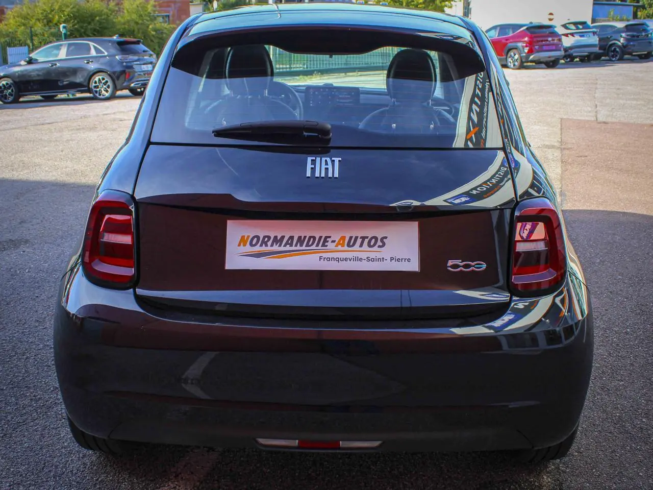 Vue arrière d'une Fiat 500 électrique noire avec logos FIAT et 500, stationnée en extérieur.
