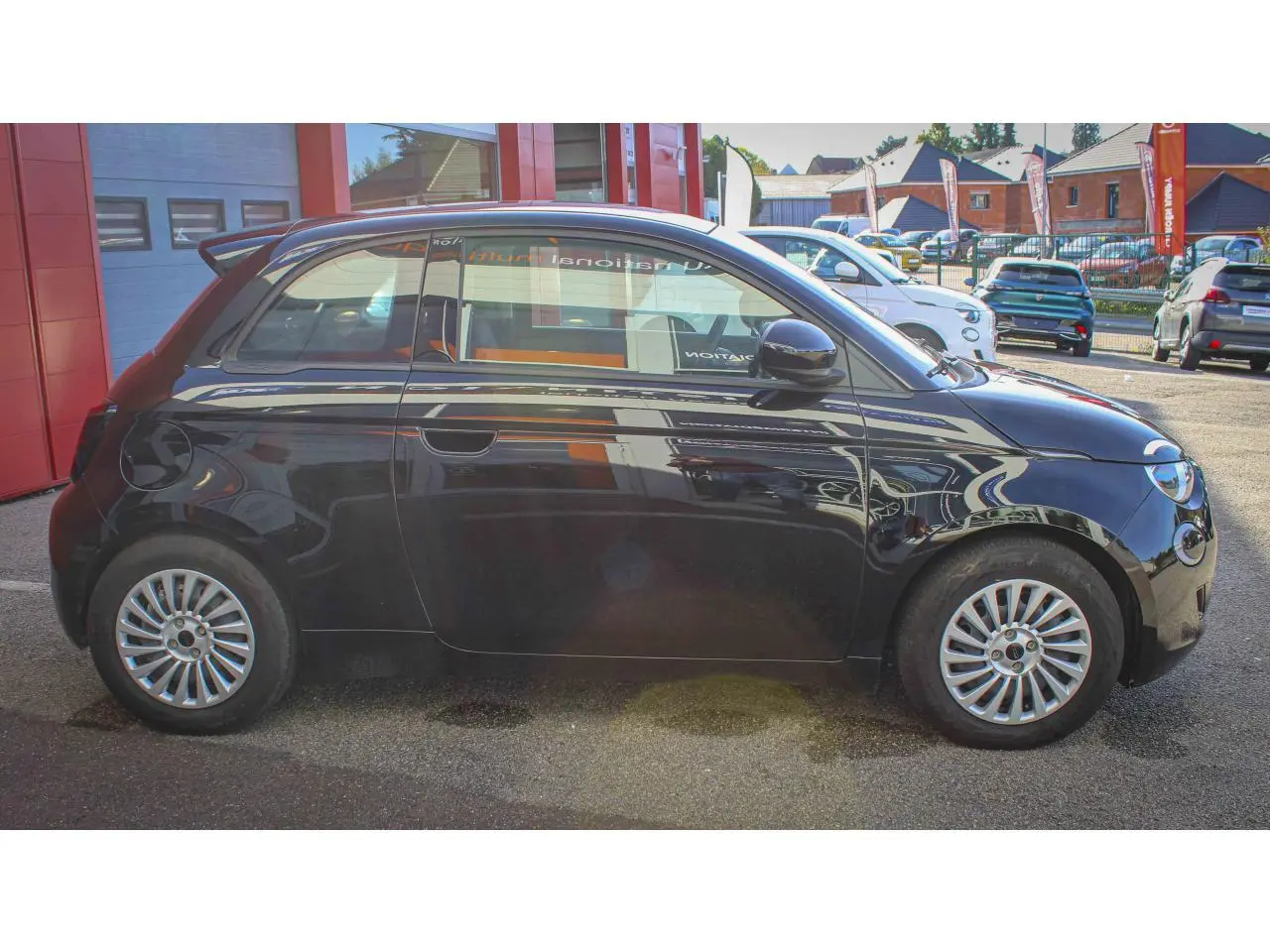 Profil côté gauche de la Fiat 500 électrique 2023 noire, avec jantes alliage et poignées de portes dissimulées.