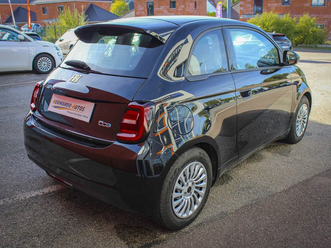 Vue 3/4 arrière droite de la Fiat 500 électrique noire 2023 avec jantes alliage et logos chromés distinctifs.