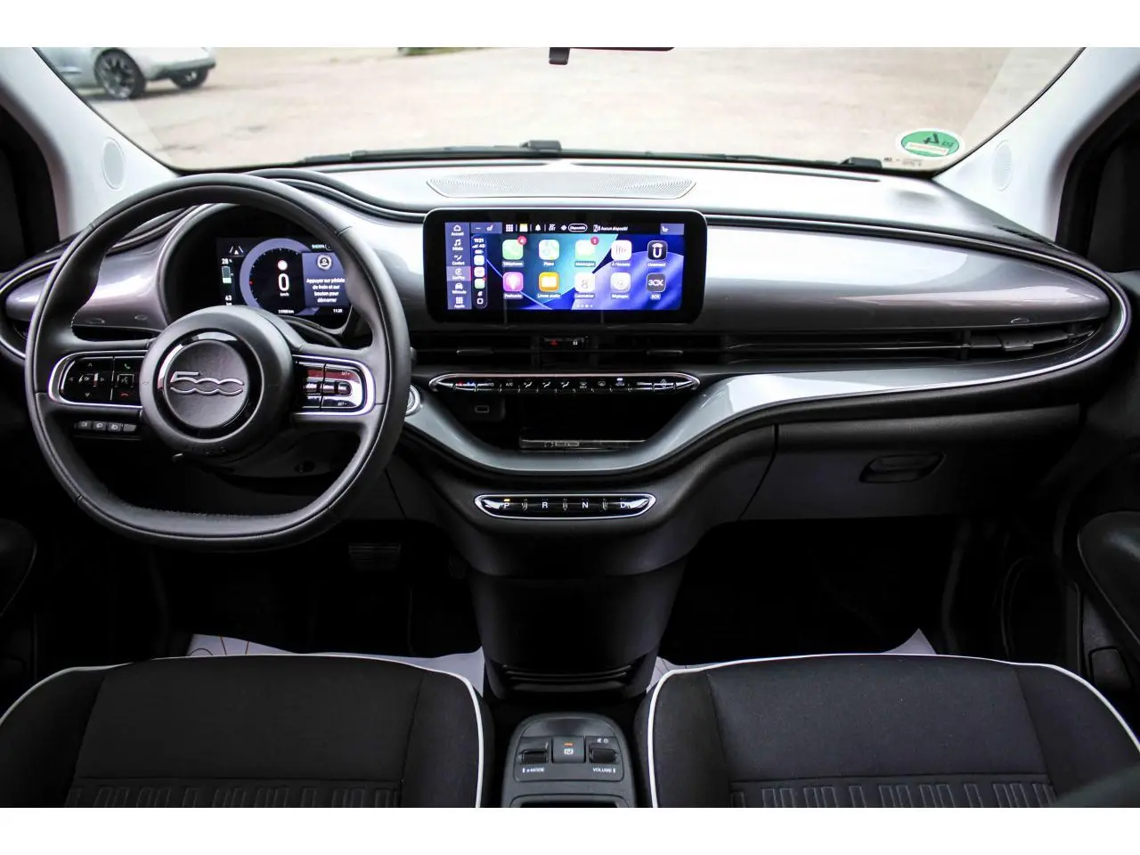 Vue intérieure frontale du tableau de bord noir de la Fiat 500 électrique 2023 avec écran tactile central et volant multifonction.