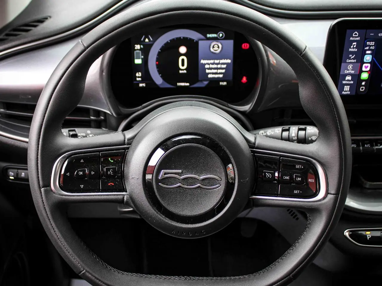 Vue rapprochée du volant noir de la Fiat 500 électrique 2023 avec commandes intégrées et tableau de bord numérique.