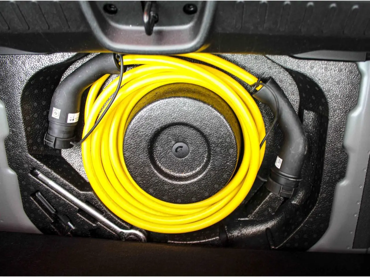 Câble de recharge électrique jaune enroulé dans le coffre de la Fiat 500 électrique noire 2023.