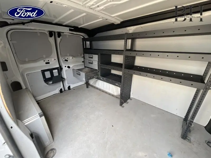 Intérieur du fourgon blanc banquise vu de l'arrière, avec étagères métalliques et rangements intégrés sur la paroi droite