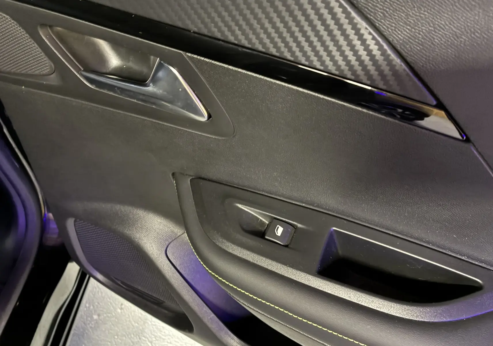 Détail de la porte intérieure côté gauche du Peugeot 2008 noir, avec poignée chromée et bouton de commande de vitre.