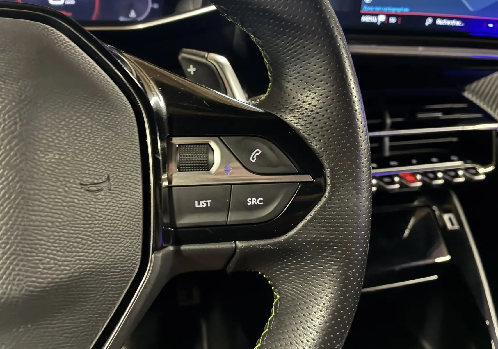 Gros plan sur la partie gauche du volant en cuir perforé du Peugeot 2008 GT Line 2020, avec commandes intégrées et tableau de bord numérique en arrière-plan.