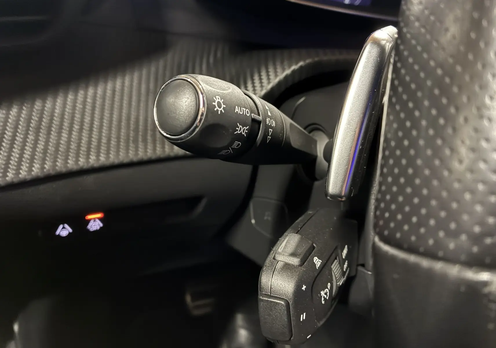 Gros plan sur les commandes de phares et régulateur au volant perforé du Peugeot 2008 noir version GT Line 2020.