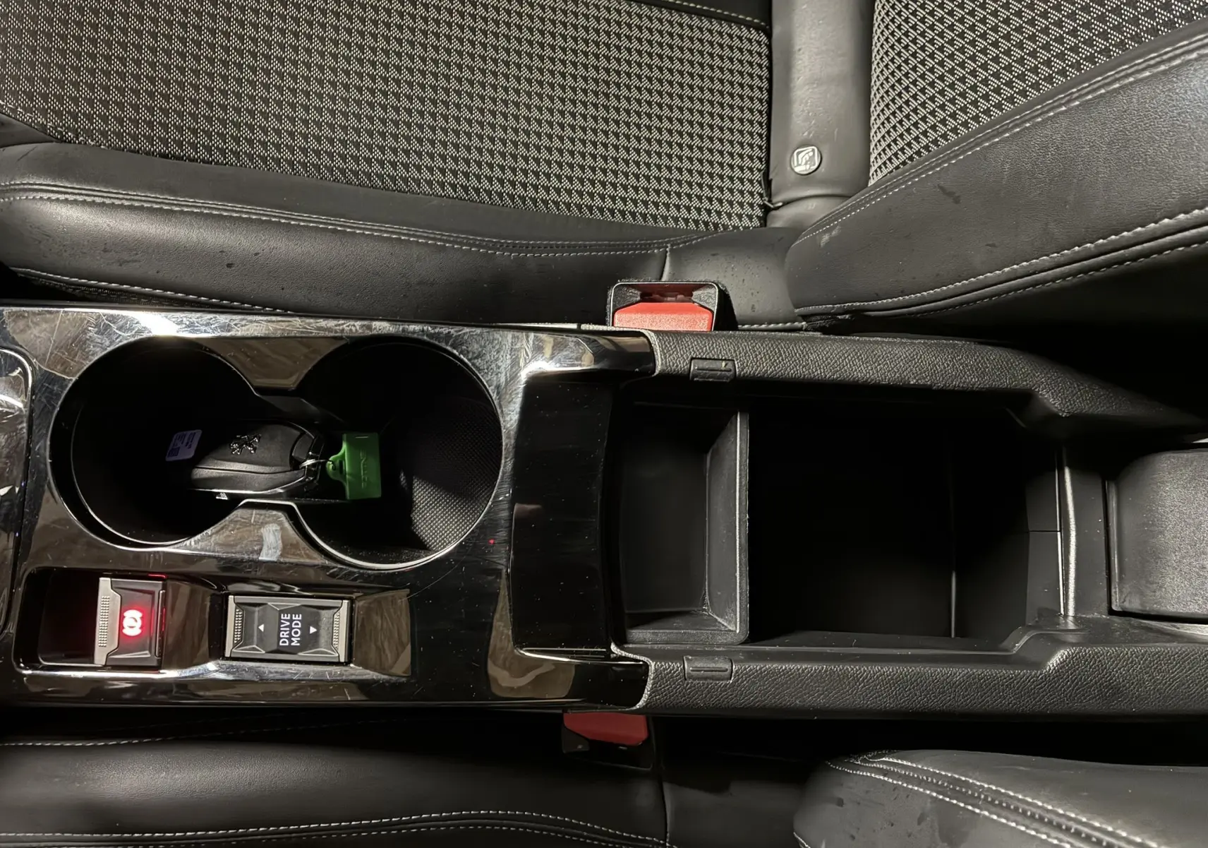 Vue rapprochée de la console centrale noire du Peugeot 2008 1.5 BlueHDi 130 GT Line avec porte-gobelets et rangement ouvert.