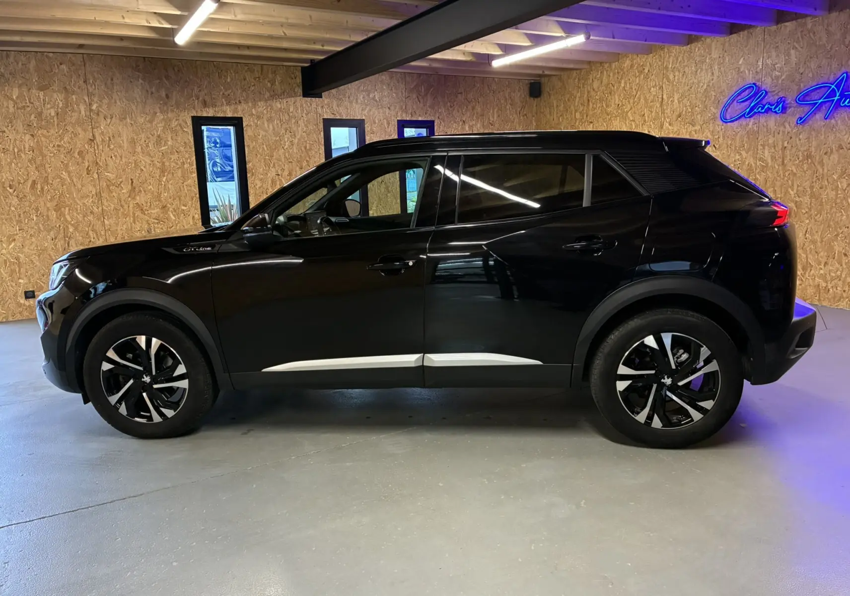 Peugeot 2008 noir vue de profil côté gauche, avec jantes bi-ton et détails GT Line sous un éclairage intérieur.