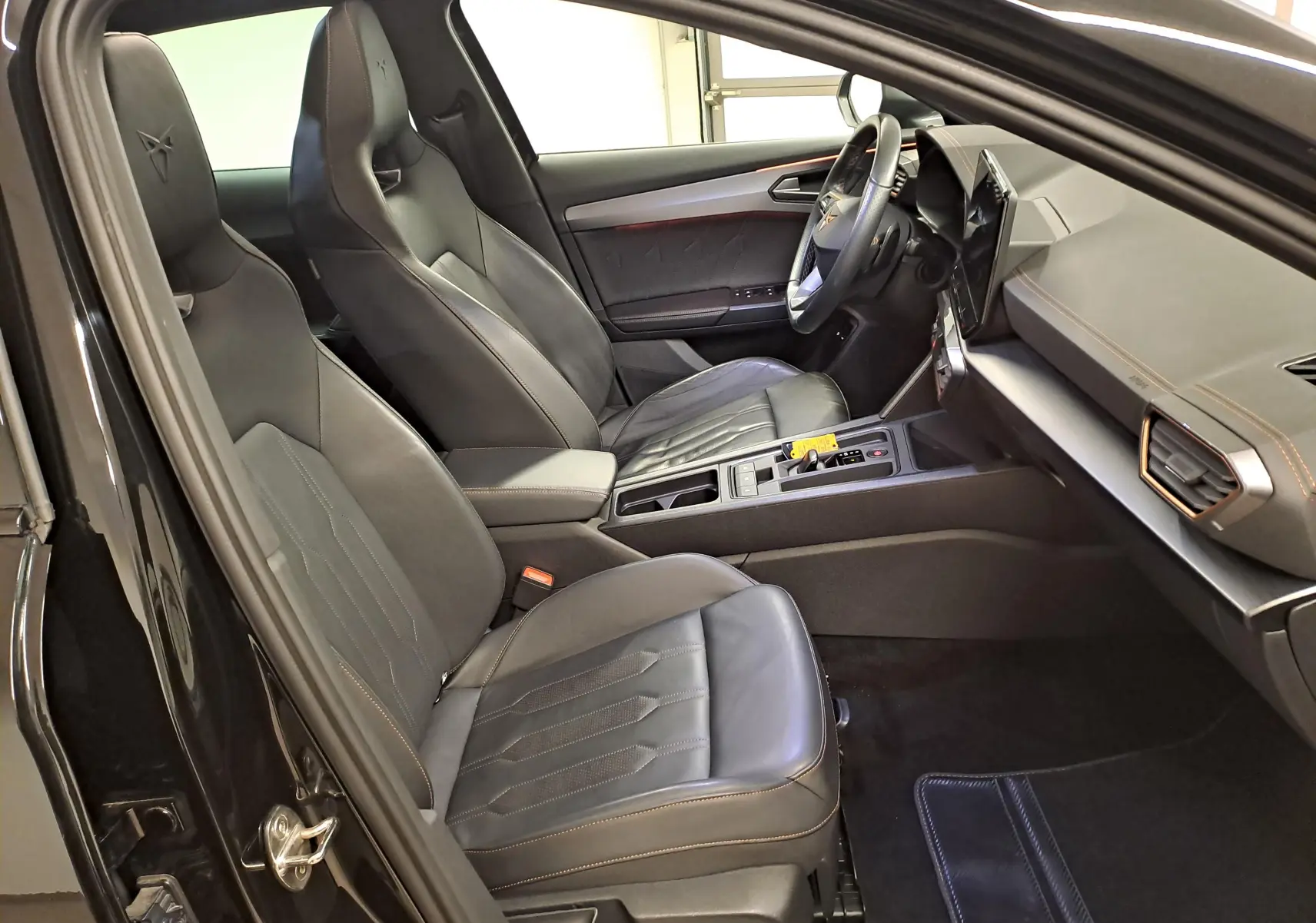 Vue intérieure côté conducteur du CUPRA Formentor 1.4 e-HYBRID 2023, sièges baquets cuir noir avec surpiqûres copper et tableau de bord moderne.