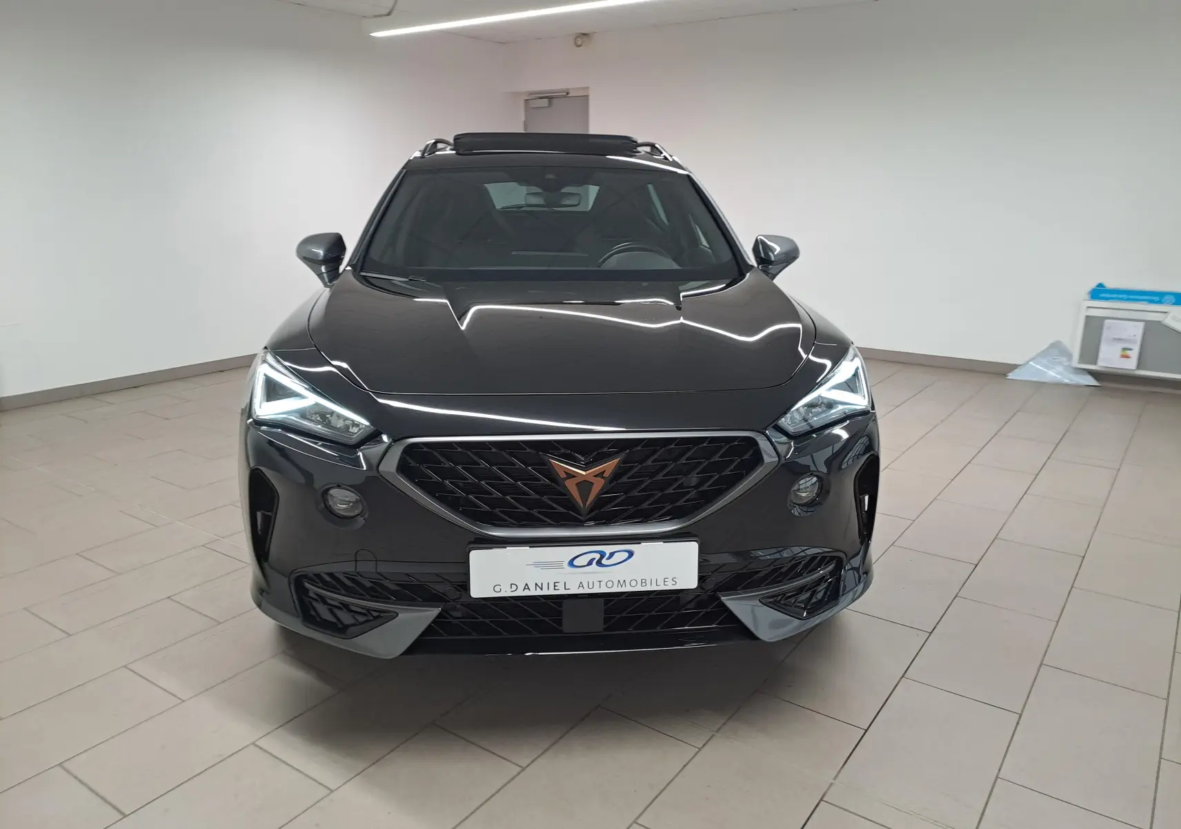 Vue frontale d'un CUPRA Formentor noir minuit 2023 avec calandre marquée et phares LED allumés dans un showroom.