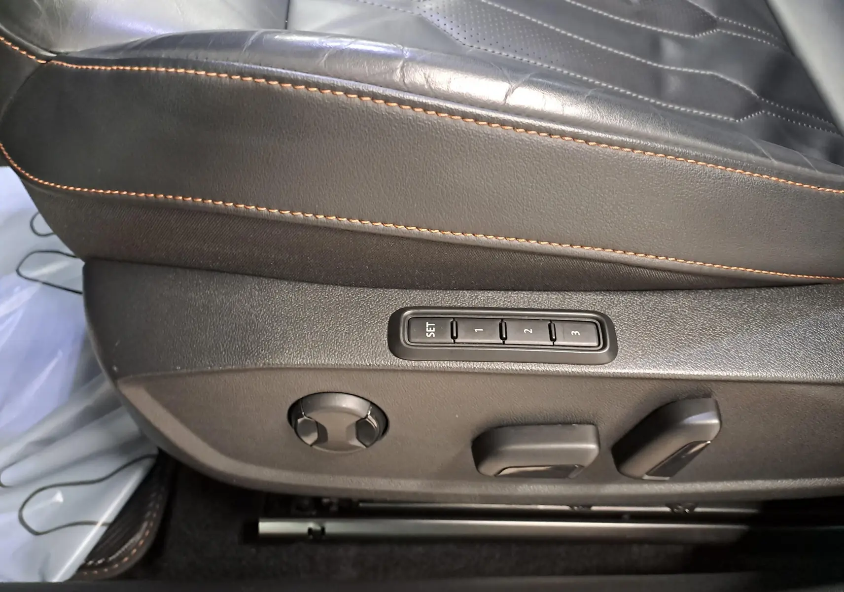 Détail du siège baquet en cuir noir Asphalte avec surpiqûres copper et commandes électriques de réglage.