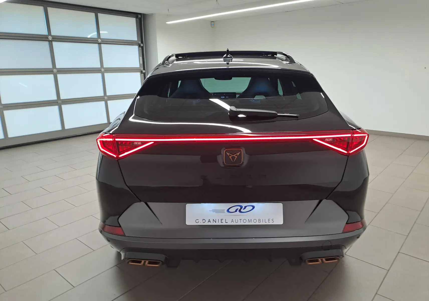 Vue arrière d'un CUPRA Formentor 1.4 e-HYBRID noir minuit avec feux LED allumés et double sortie d'échappement cuivrée.