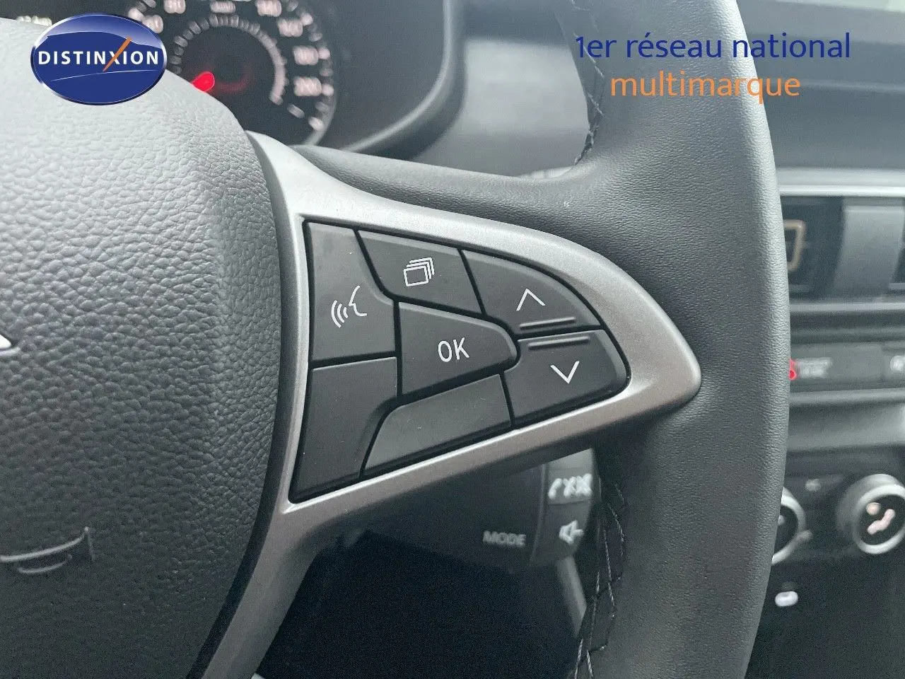 Gros plan sur le volant noir avec commandes multifonctions du Dacia Jogger gris schiste, tableau de bord en arrière-plan.