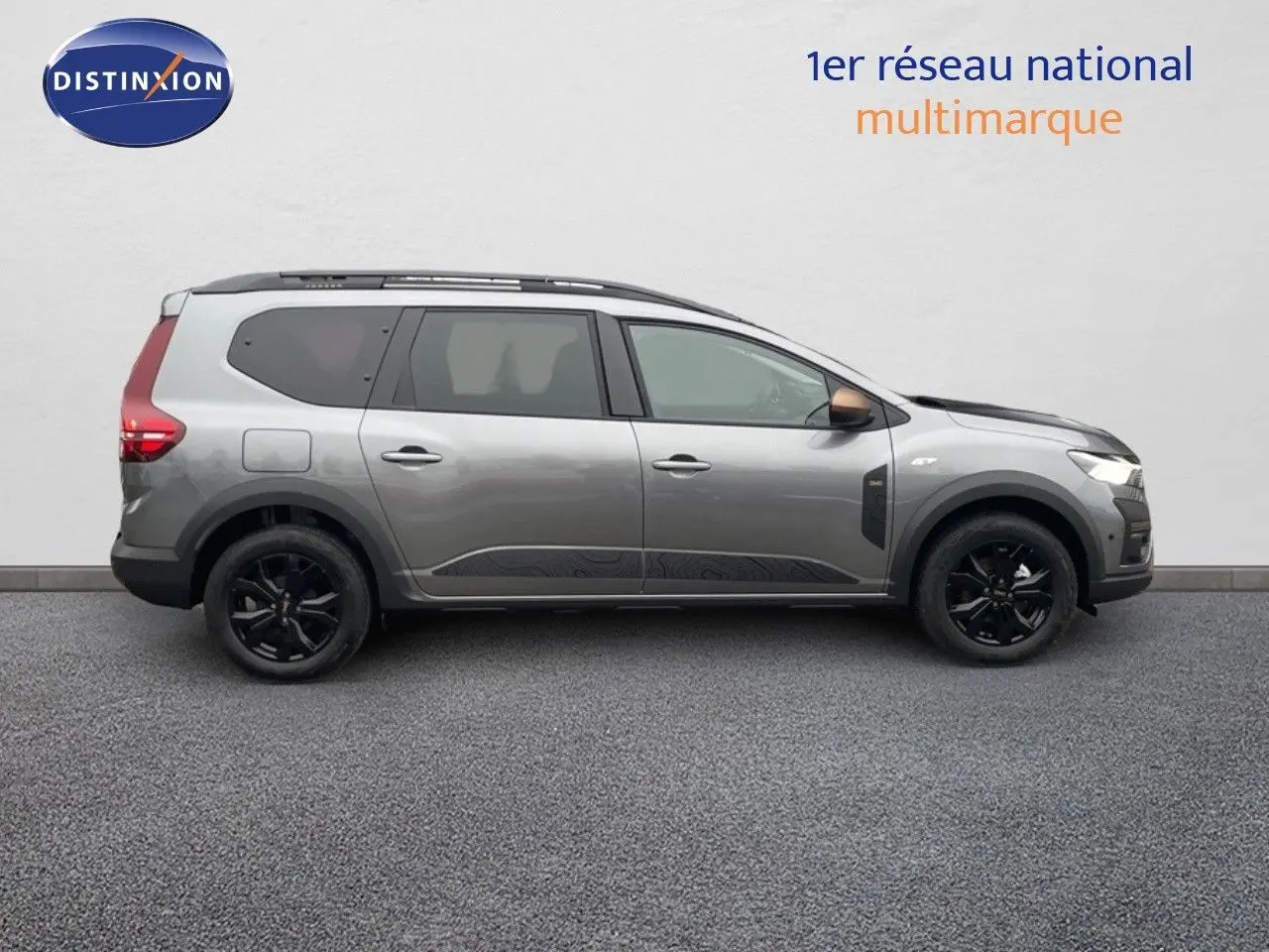 Vue de profil côté gauche d'un Dacia Jogger gris schiste métal avec jantes noires et toit équipé de barres de toit.