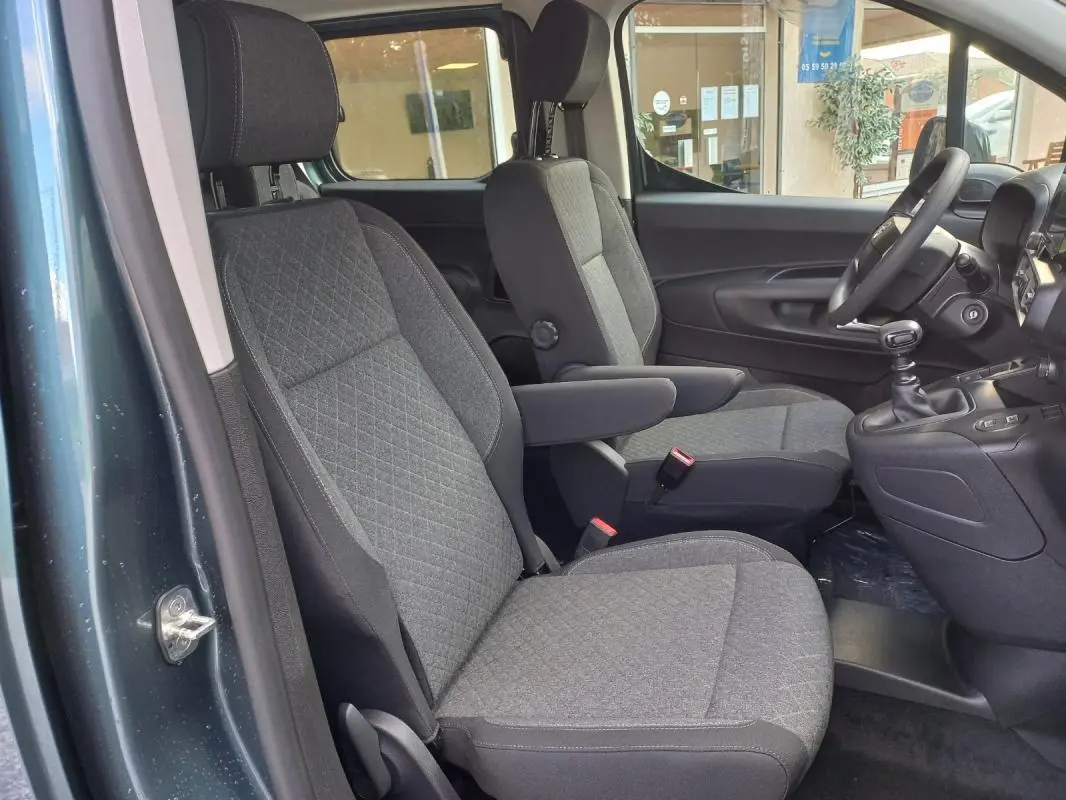 Vue intérieure côté gauche de l’Opel Combo Life Elegance M 2025 bleu, montrant les sièges avant en tissu gris et la boîte manuelle.