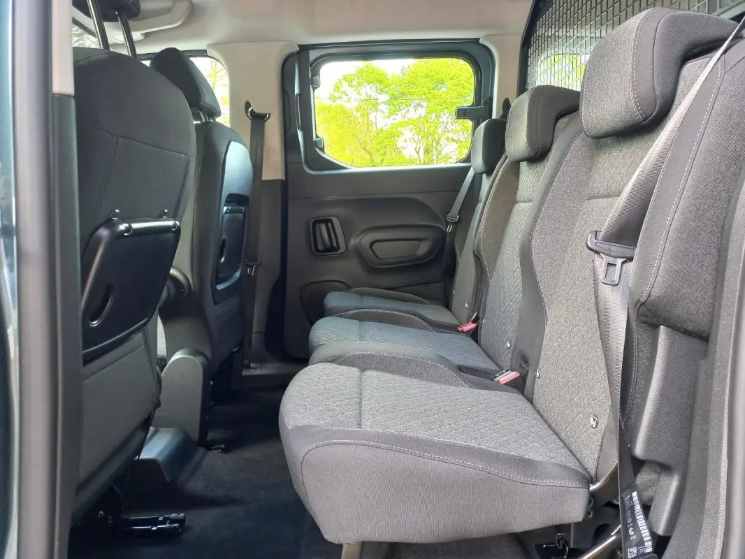 Vue latérale intérieure sur les sièges arrière gris du Opel Combo LIFE Elegance M 2025, avec tablette rabattable au dos des sièges avant.