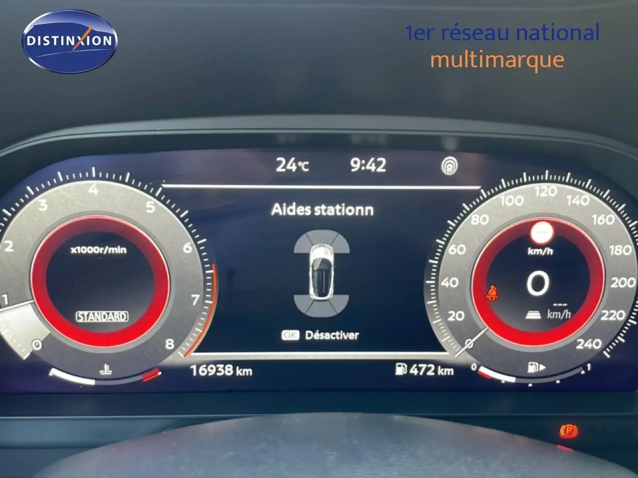Tableau de bord numérique du Nissan Juke noir, affichant les aides au stationnement et compteurs à aiguille rouges.
