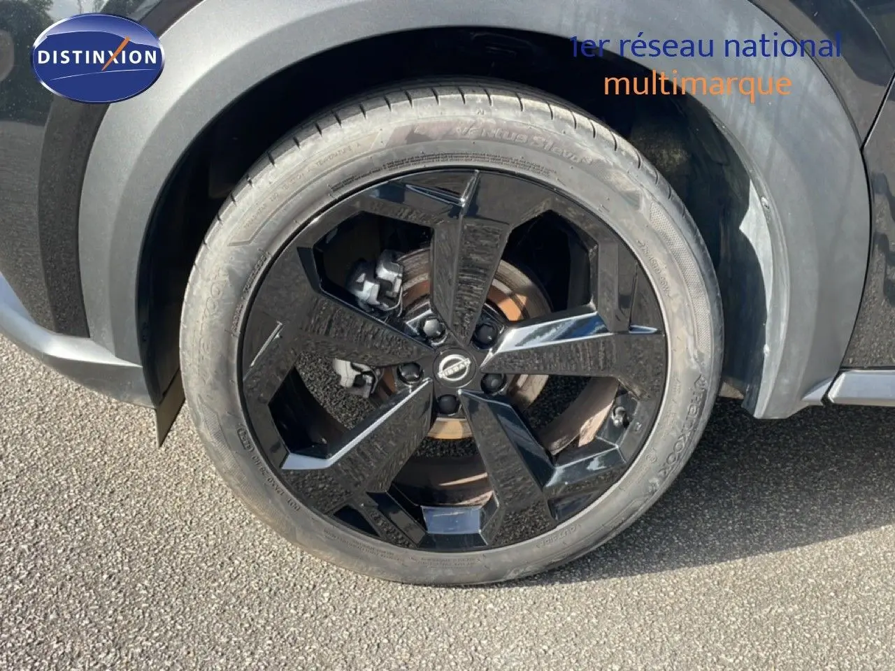 Gros plan sur la roue avant gauche noire brillante du Nissan Juke 2025 en finition Tekna, avec carrosserie noir Kuro Metal.