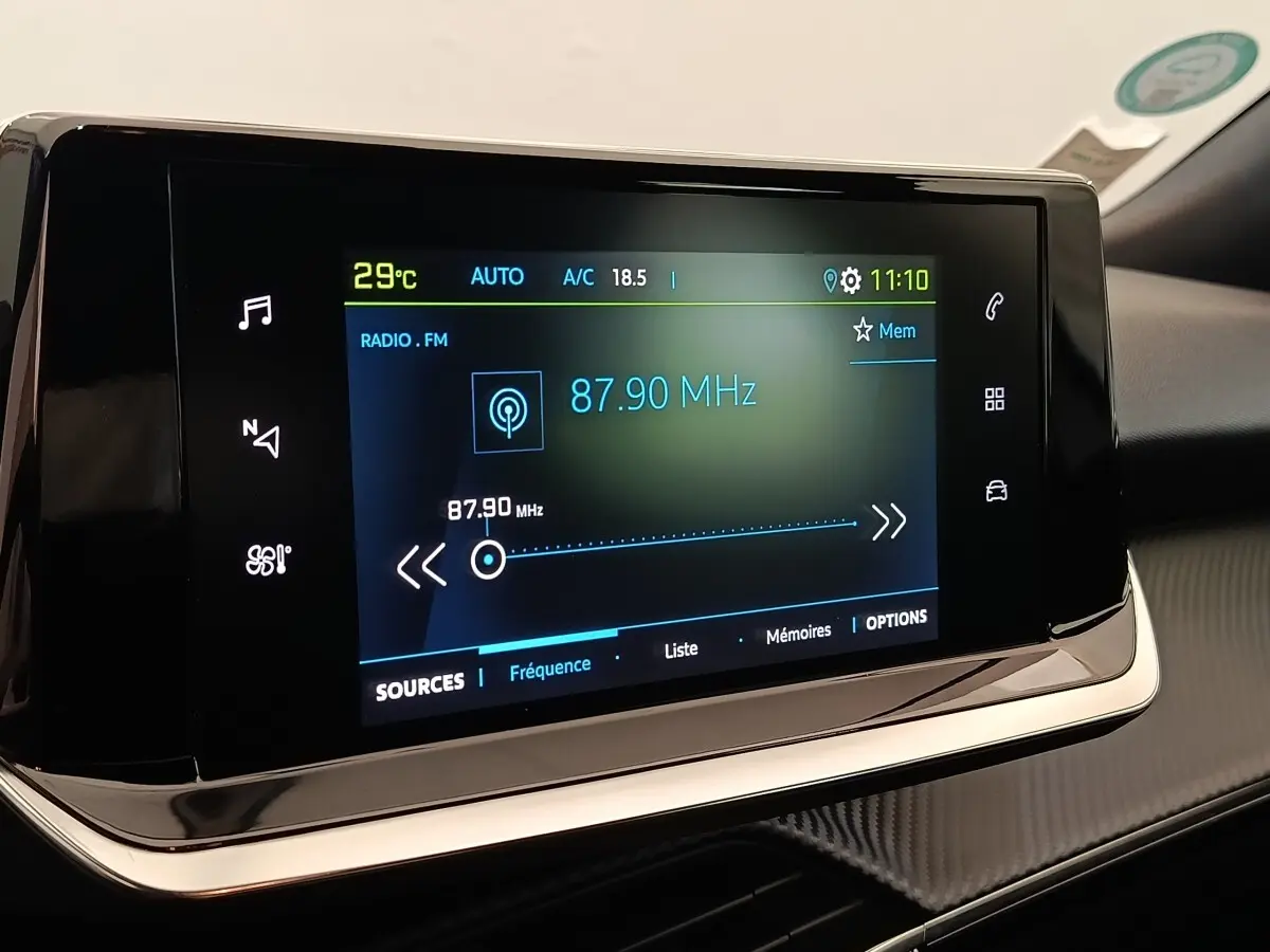 Écran tactile central du tableau de bord du Peugeot E-2008 électrique, affichant la radio FM à 87,90 MHz.
