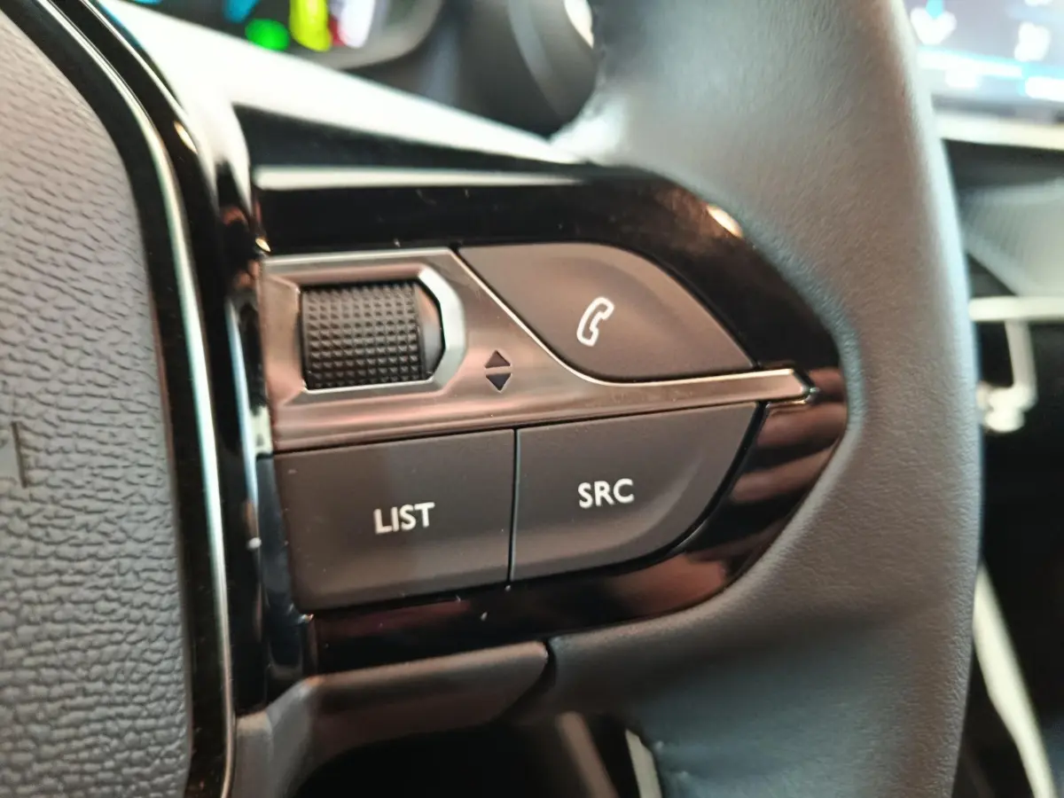 Gros plan sur les commandes multifonctions en cuir du volant côté gauche du Peugeot E-2008 électrique gris clair.