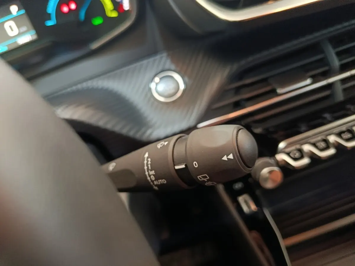 Gros plan sur la commande d’essuie-glace à gauche du volant dans l’habitacle noir du Peugeot E-2008 électrique gris clair.