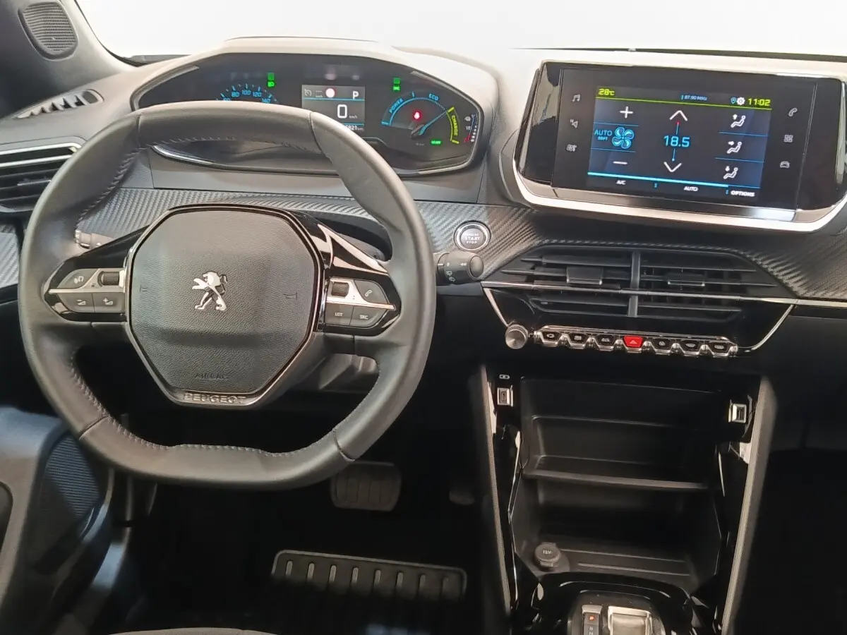 Vue intérieure centrée sur le volant cuir multifonctions et le tableau de bord numérique du Peugeot E-2008 électrique gris.