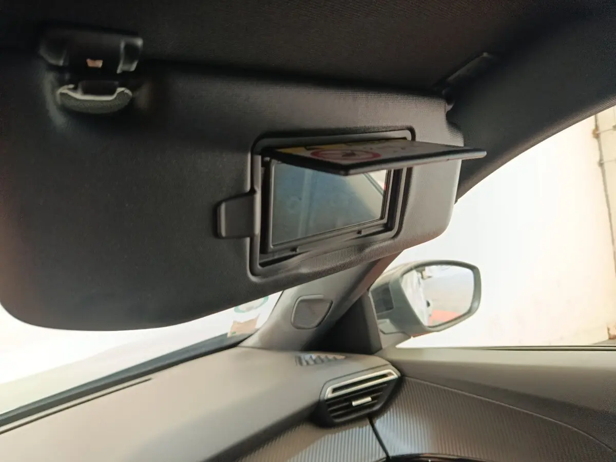 Vue intérieure côté passager du Peugeot E-2008 électrique gris clair, avec pare-soleil et miroir de courtoisie ouverts.
