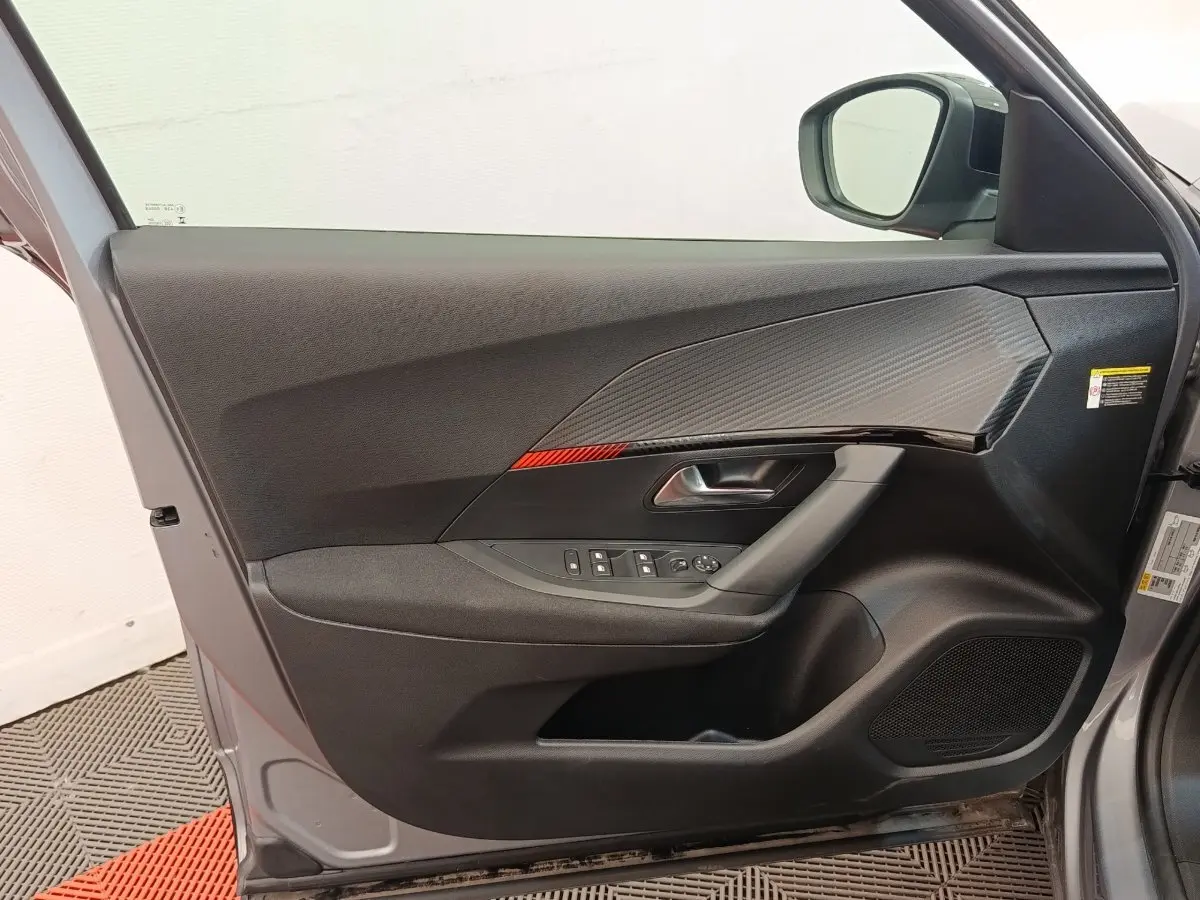 Vue intérieure de la porte avant gauche gris clair du Peugeot E-2008 électrique avec insert carbone et commandes fenêtres.