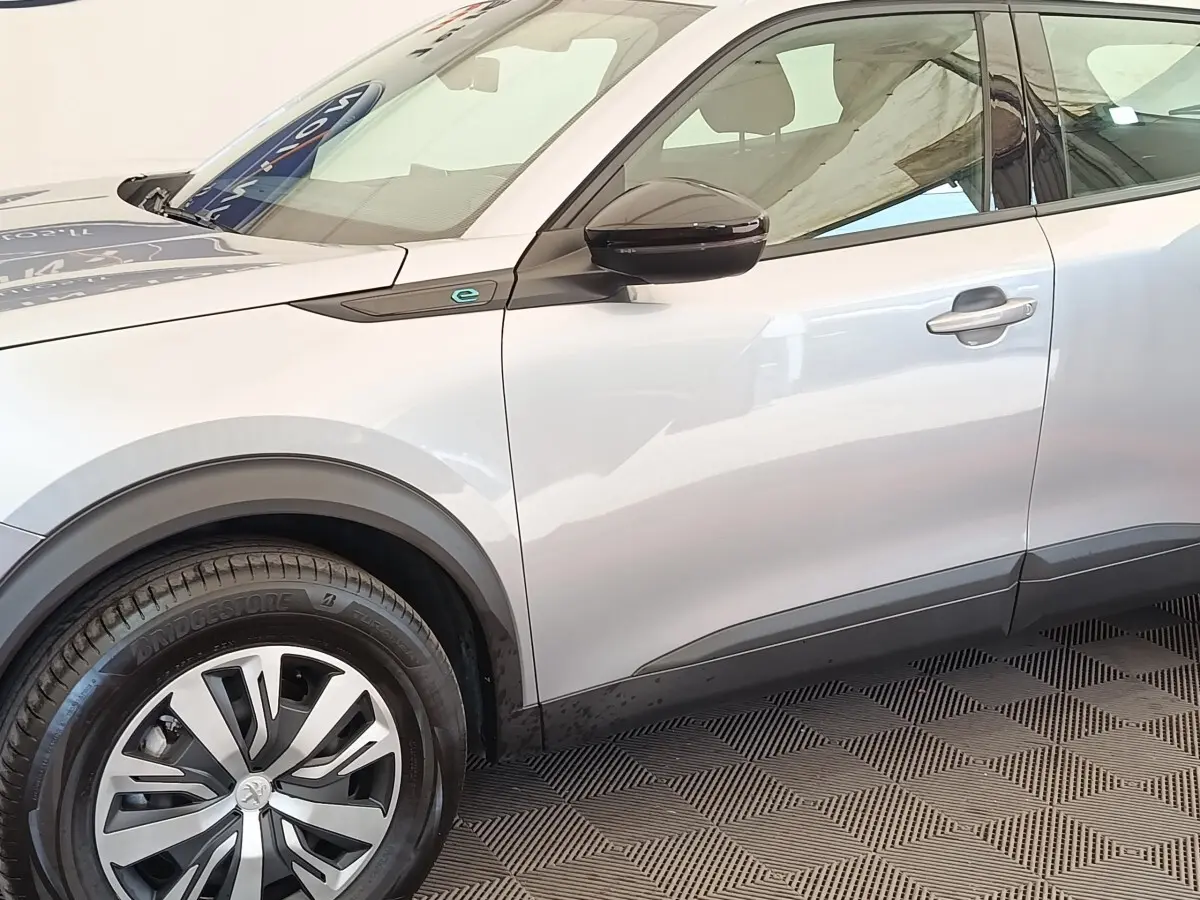 Vue de profil côté gauche du Peugeot E-2008 électrique gris clair avec jante et rétroviseur noir brillant.