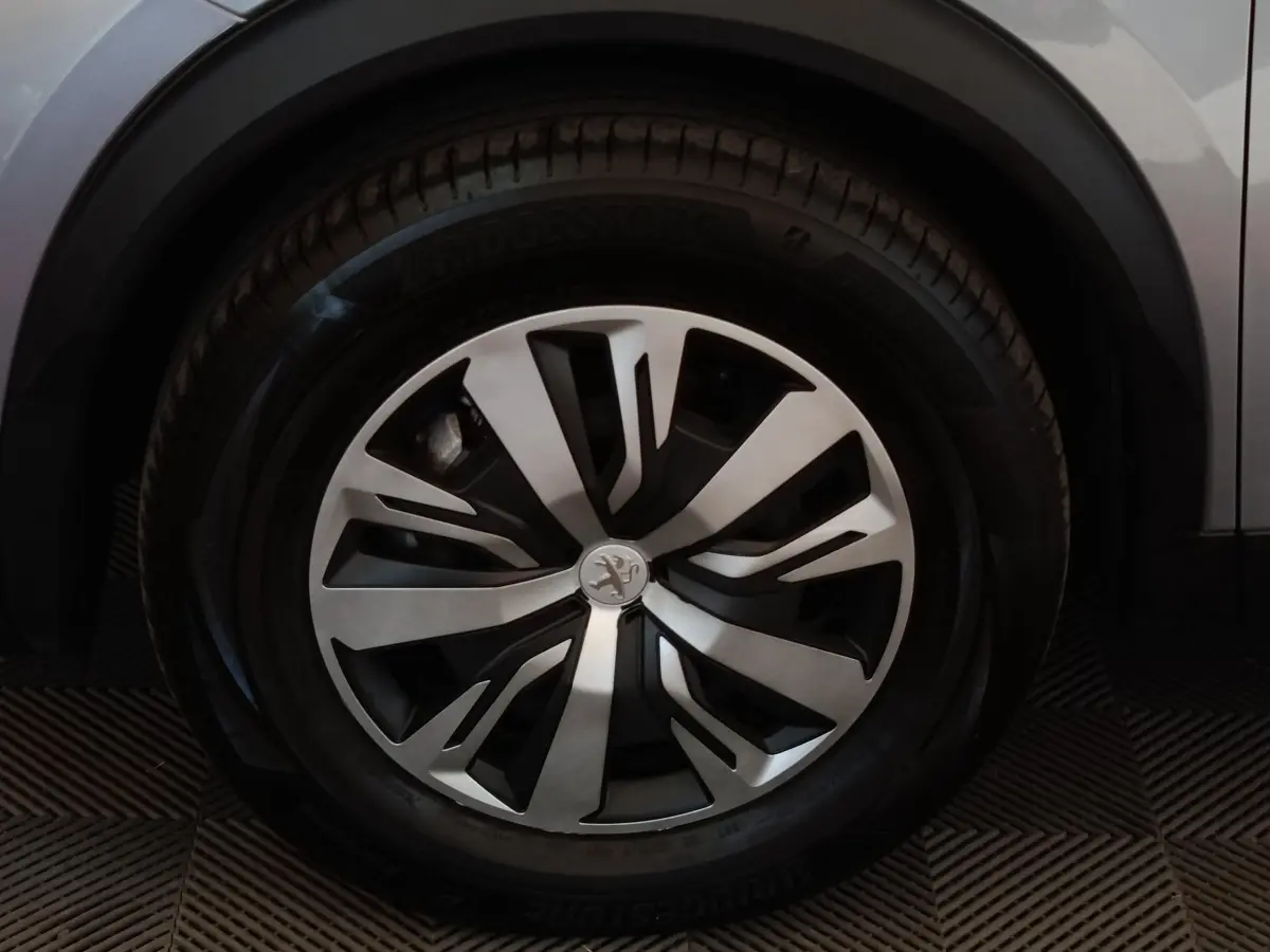 Gros plan sur la roue avant droite du Peugeot E-2008 électrique gris clair avec jante alliage au design moderne.