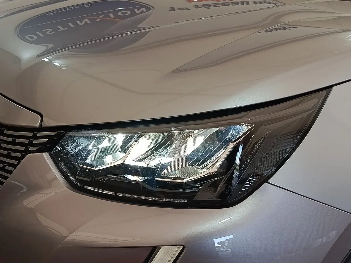 Gros plan sur le phare avant droit du Peugeot E-2008 électrique gris clair, mettant en valeur les détails LED et la calandre.