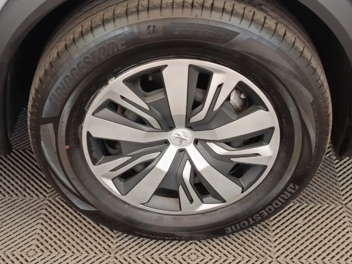 Gros plan sur la roue avant droite de la Peugeot E-2008 électrique gris clair avec jante alliage et logo lion central.