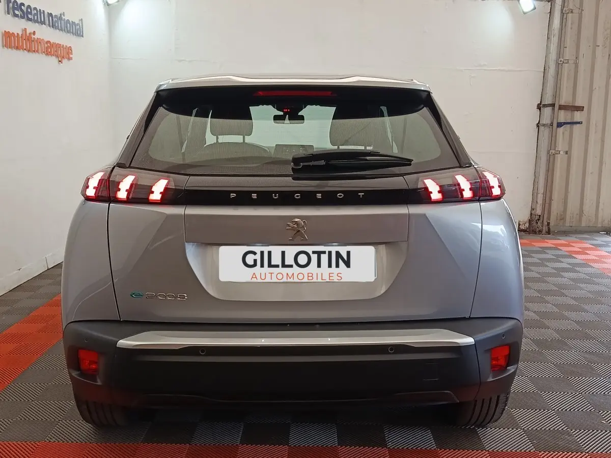 Vue arrière d'un Peugeot E-2008 électrique gris clair avec feux LED caractéristiques allumés en intérieur.