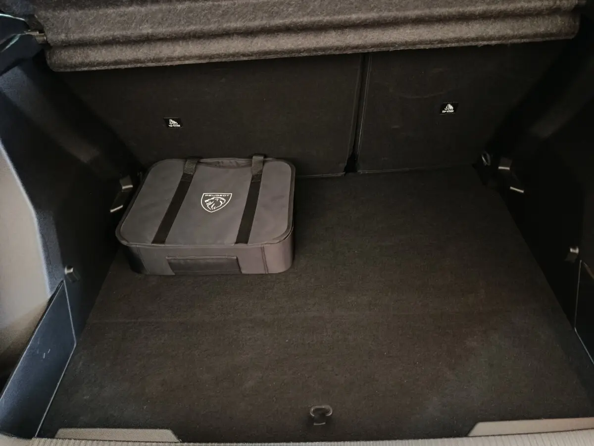Coffre spacieux de Peugeot E-2008 électrique gris clair avec sac de rangement Peugeot posé au sol.