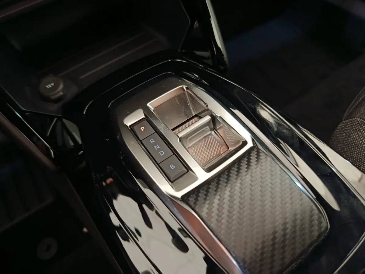 Gros plan sur la console centrale noire brillante avec sélecteur de vitesses électronique du Peugeot E-2008 électrique gris clair.