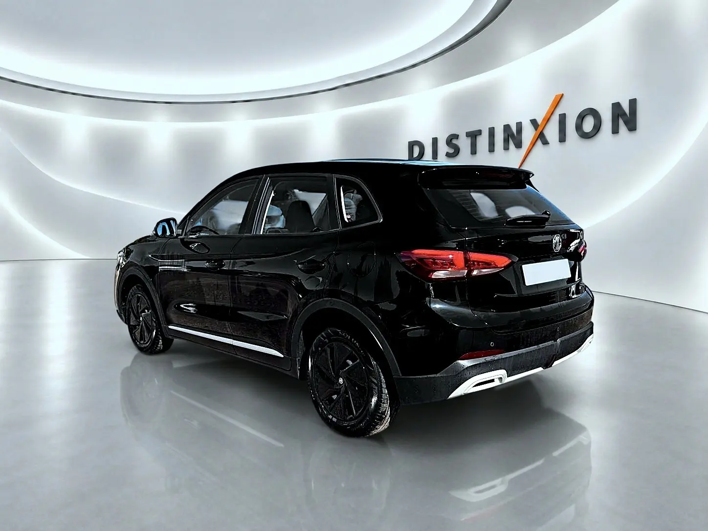 Vue 3/4 arrière droite du SUV MG ZS 1.5 hybrid noir brillant avec jantes noires dans un showroom moderne.