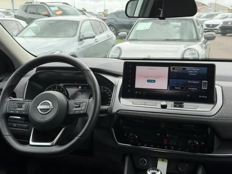 Vue intérieure du tableau de bord du Nissan Qashqai blanc nacré 2025, avec écran tactile et volant multifonction cuir.