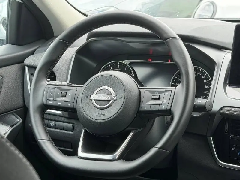 Vue rapprochée du volant cuir noir multifonction du Nissan Qashqai 2025 avec tableau de bord digital en arrière-plan.