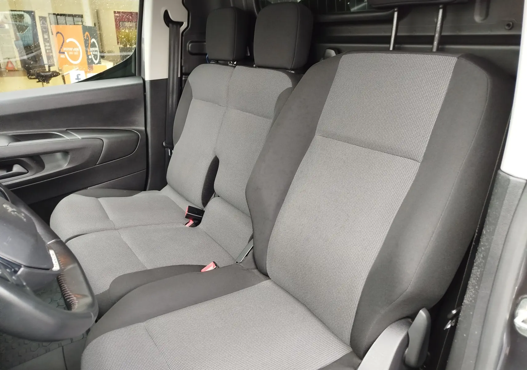 Vue intérieure côté conducteur du Peugeot Partner 2020, montrant les sièges gris clair et foncé en tissu.