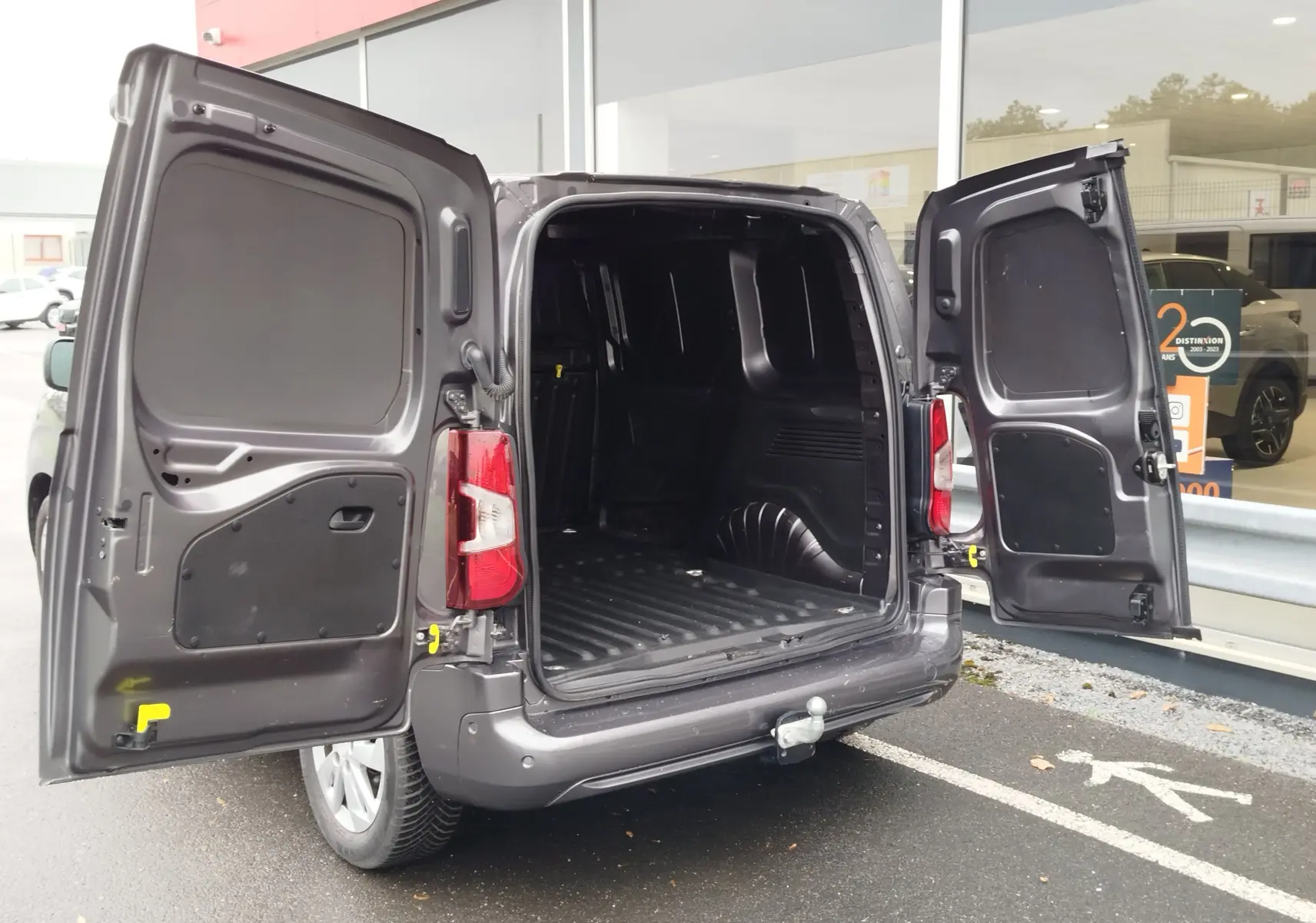 Vue arrière 3/4 droit d'un Peugeot Partner gris foncé avec portes arrière ouvertes montrant l'espace de chargement vide.