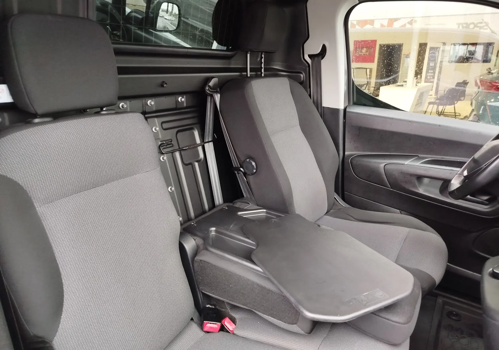 Vue intérieure côté droit du Peugeot Partner 2020 gris foncé, montrant les sièges avant et une tablette rabattable centrale.