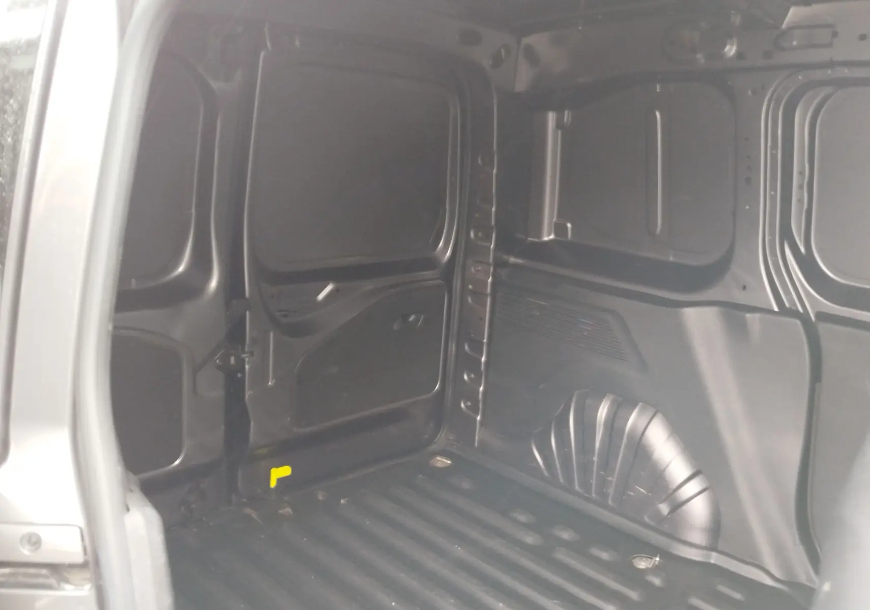 Vue intérieure de la zone de chargement du Peugeot Partner gris foncé, montrant les parois métalliques et le plancher strié.