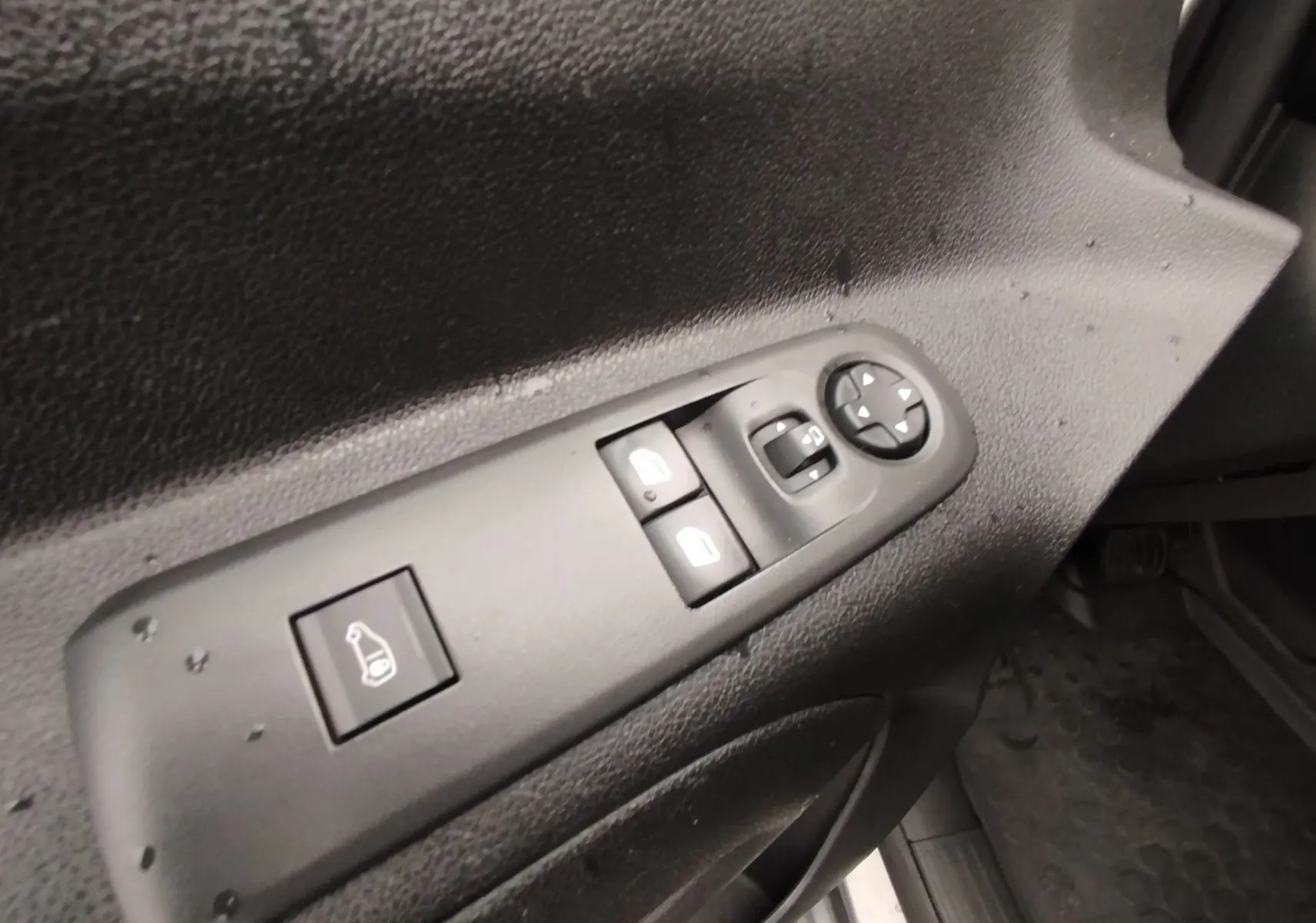 Gros plan sur les commandes de réglage des vitres et des rétroviseurs côté conducteur du Peugeot Partner gris foncé 2020.