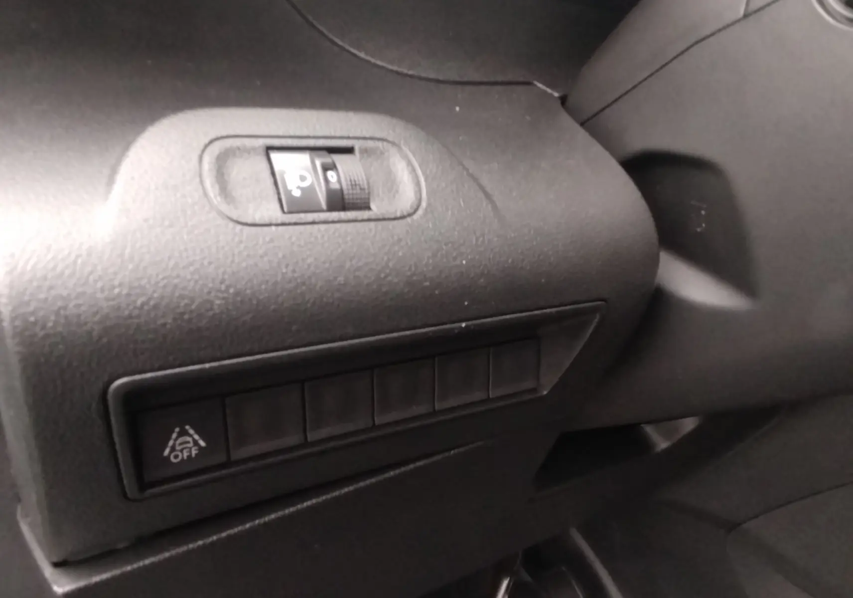 Détail intérieur montrant les commandes de réglage des phares et l'activation du système d'alerte de franchissement de ligne sur Peugeot Partner gris.