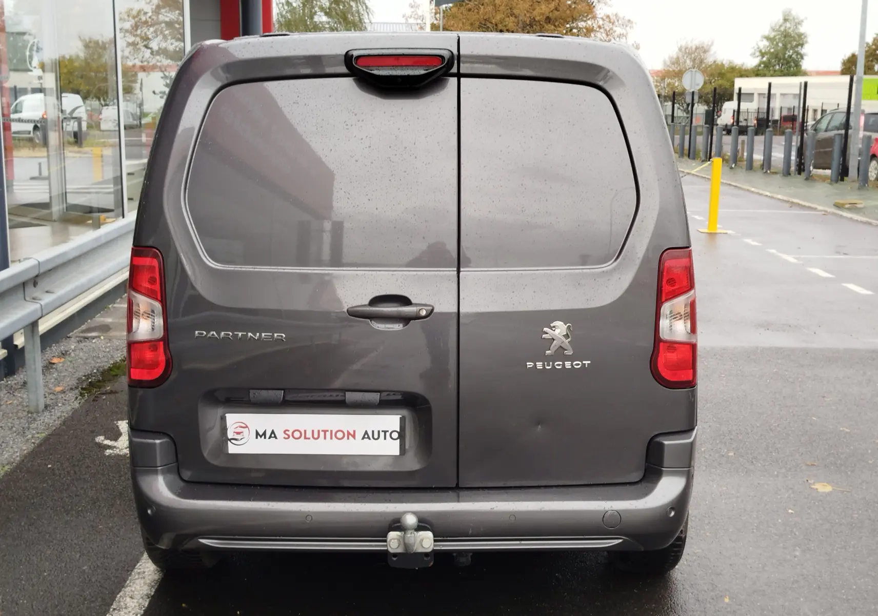 Vue arrière d'un Peugeot Partner gris foncé 2020 avec portes battantes et attelage de remorque visible.