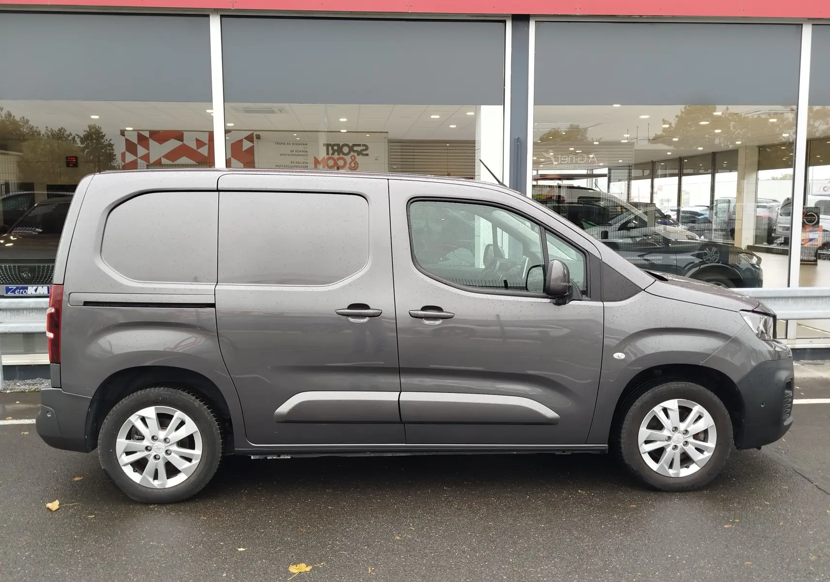 Vue de profil côté gauche d'un Peugeot Partner gris foncé 2020, utilitaire compact avec porte latérale coulissante.