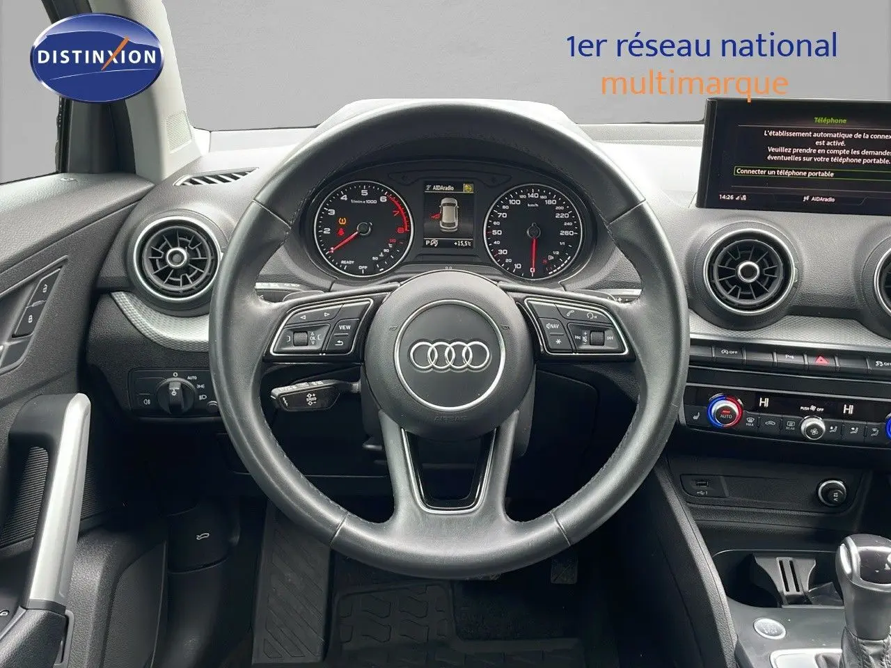 Vue frontale du poste de conduite de l'Audi Q2 noir mito metal 2023 avec volant multifonction et tableau de bord digital.