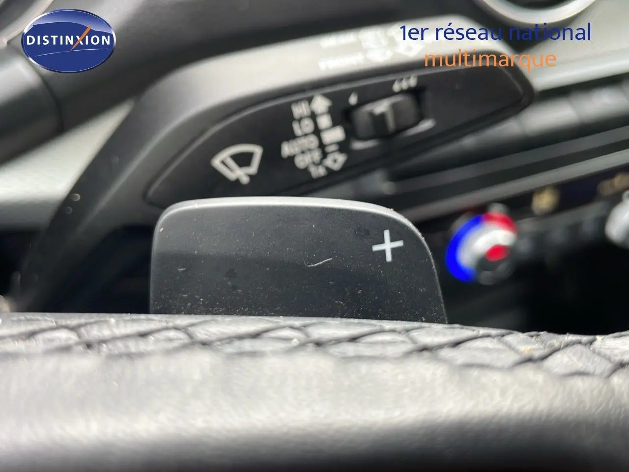 Gros plan sur la palette de passage de vitesses droite du volant d'un Audi Q2 noir mito metal, avec commandes de climatisation en arrière-plan.